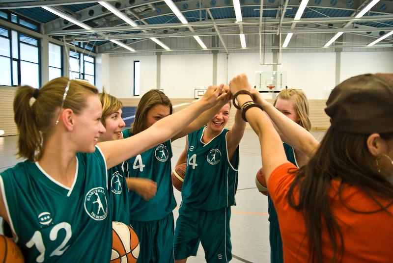 Sechs junge Basketballspielerinnen feiern mit einem Handschlag, während sie Bälle in ihren Händen halten.