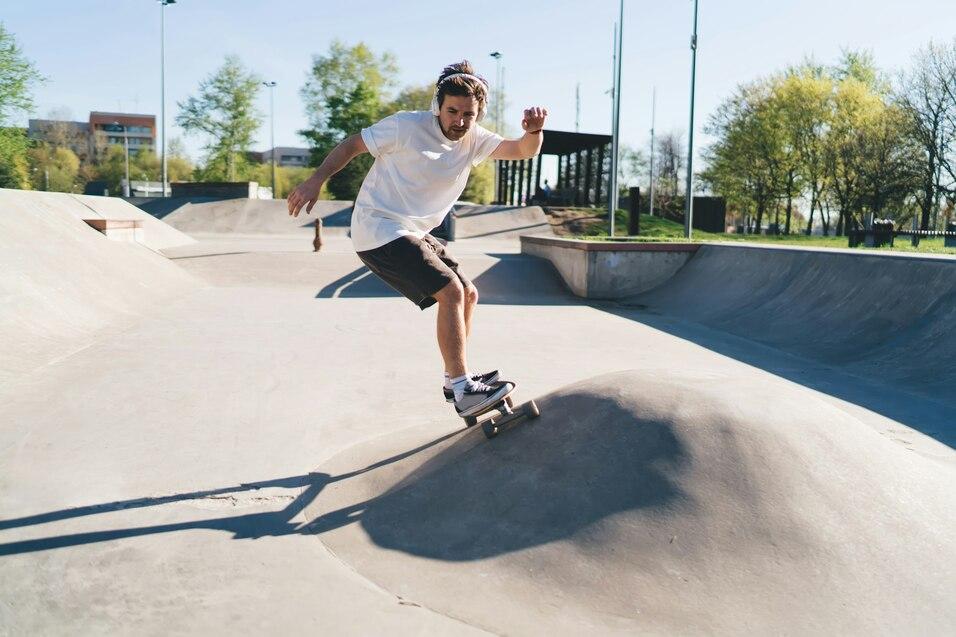 Skateboardfahrer springt über eine kleine Erhebung in einem Skatepark bei sonnigem Wetter.